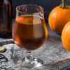 photo of a tulip snifter of porter pumpkin beer with a beer bottle, can opener, and pie pumpkins