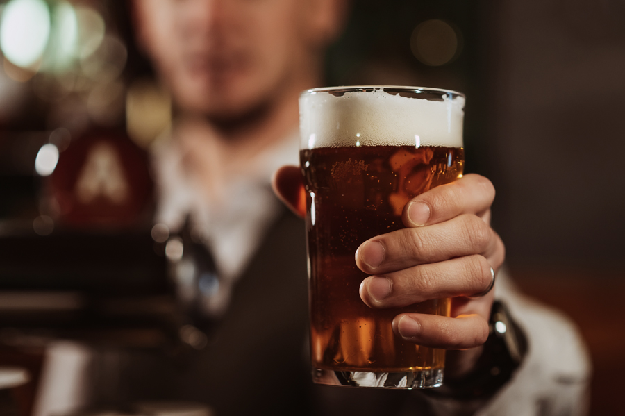 photo of bartenders hand with a glass of light draft beer with foam in bar